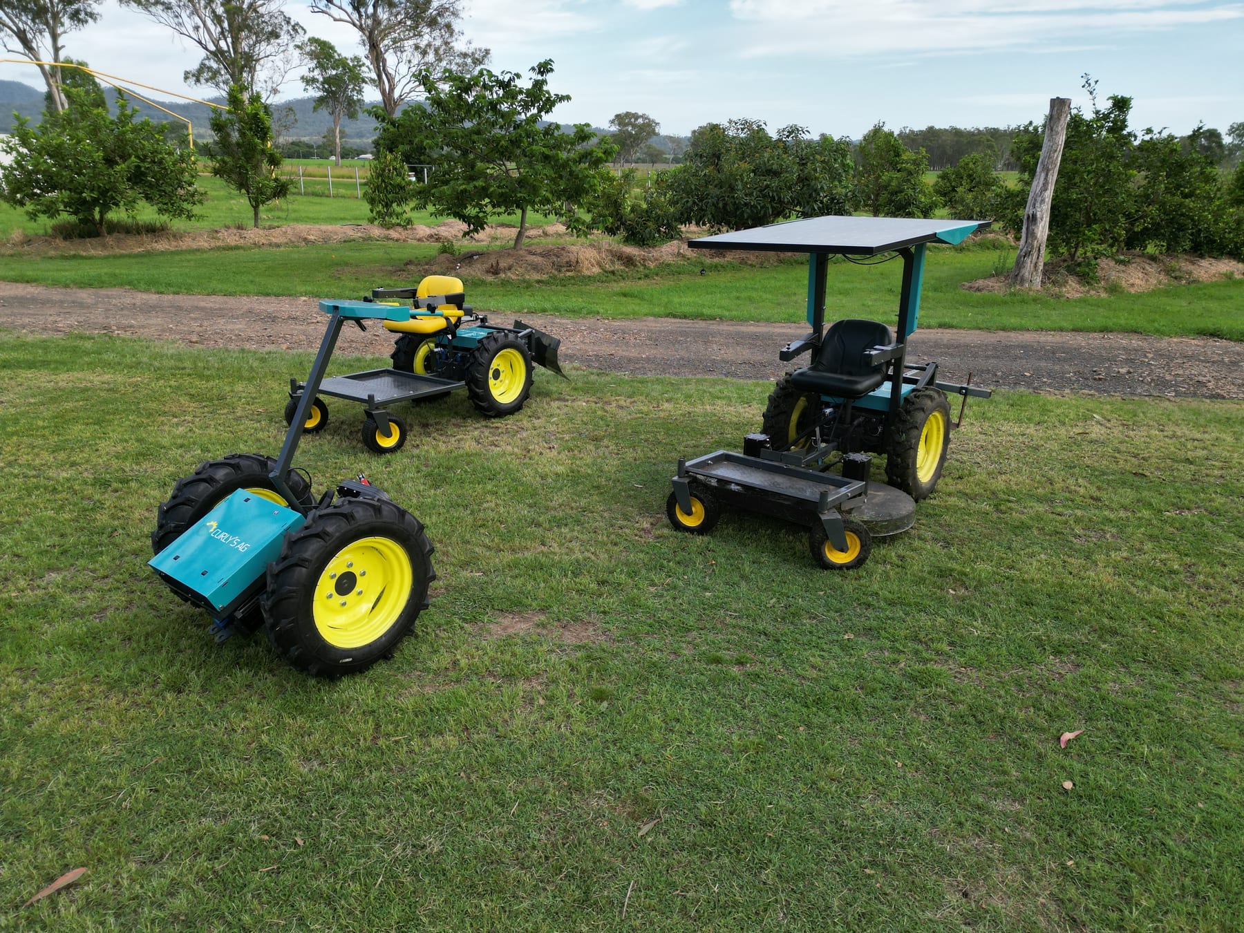 Two teal EXD electric platforms in a field — the 2-wheel Cyber Clydesdale and a larger 4-wheel solar-canopy platform