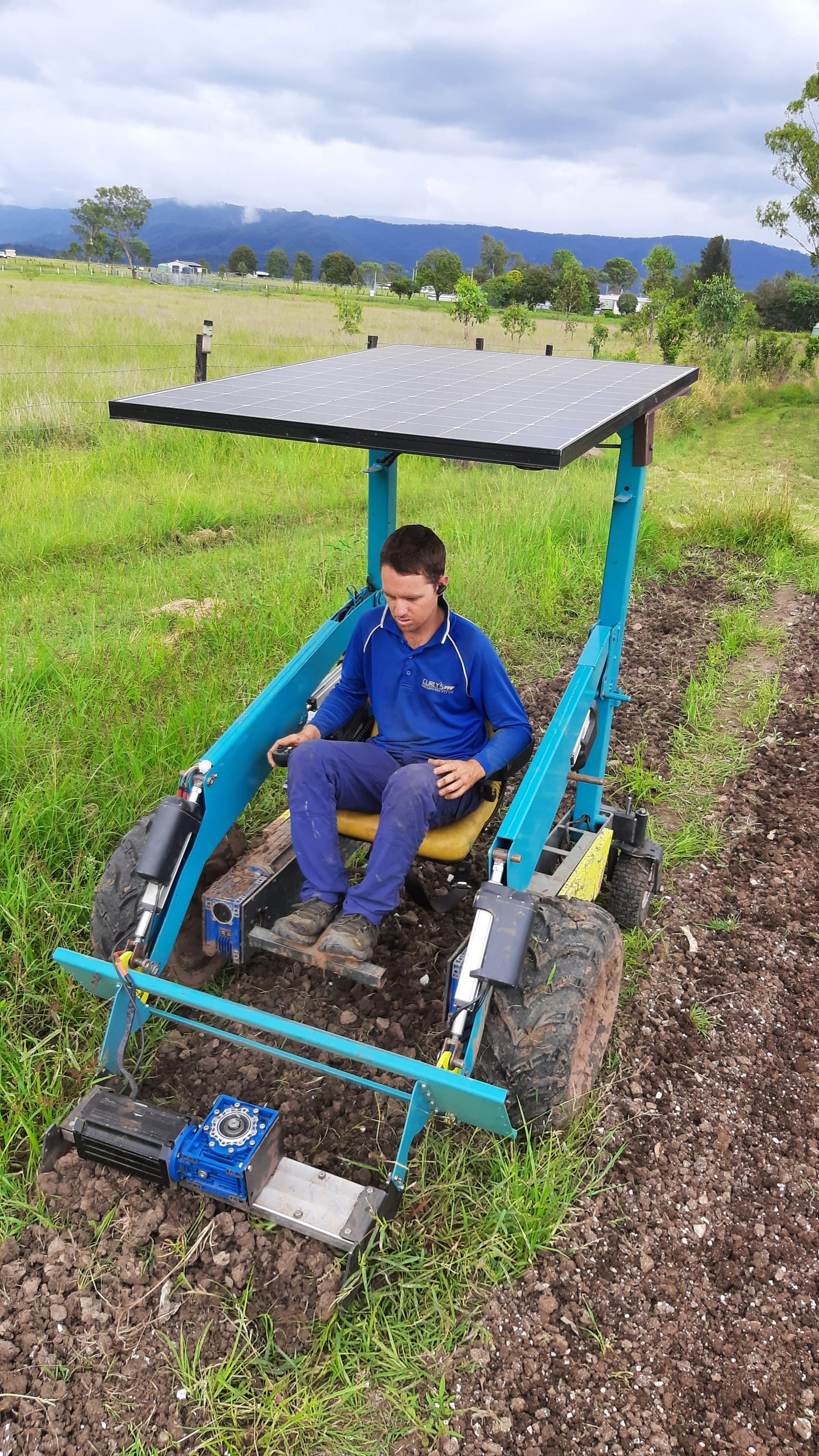 Operator driving a teal Hand-E electric platform with a solar canopy, working soil in a field
